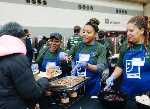Three women who chose to give back with Goodwill at last year's annual community Thanksgiving Dinner and Resource Fair. Volunteers pictured wearing Goodwill aprons while handing out food at the dinner.