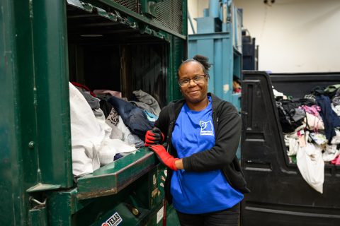 A female employee in a Goodwill Sustainability Center standing next to a machine full of clothing collected for recycling.
