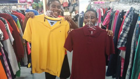 Two shoppers smiling holding up clothing items in thrift store